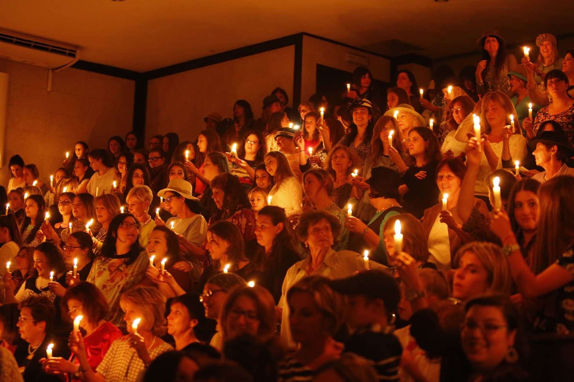 A large, joyful community gathering holding lit Shabbos candles